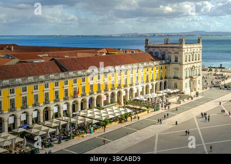 Vue panoramique sur la place du commerce ou Praca do Comercio à Lisbonne, Portugal, architecture jaune pombaline emblématique, cafés en plein air animés, fleuve Tage, vie urbaine, centre-ville historique, jour ensoleillé, ciel avec des nuages. Rayon de soleil au-dessus du bâtiment, destination de voyage Banque D'Images