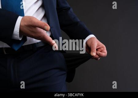 Vue rognée d'un homme d'affaires dans un costume de marine et cravate bleue, tirant une poche vide comme symbole de difficultés financières ou de faillite. Banque D'Images