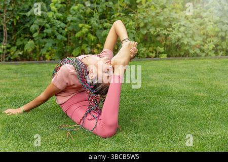Fille aux cheveux longs flexible effectuant des exercices de gymnastique dans le jardin. Horizontalement. Banque D'Images