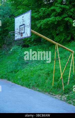 Vieux panier de basket abandonné dans un parc avec des arbres verts comme arrière-plan. Banque D'Images