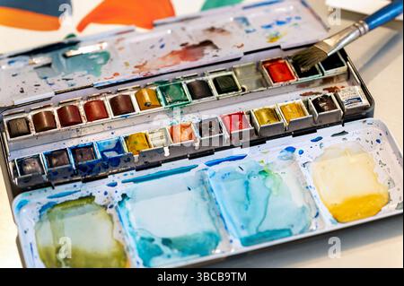 Palette d'aquarelle colorée avec pinceau reposant sur le dessus, montrant des signes de création artistique Banque D'Images