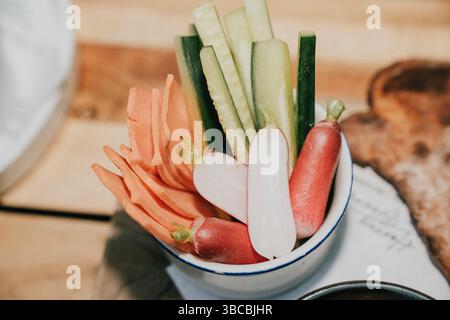 Un bol de légumes comprenant des carottes, des radis et des concombres. Le bol est sur une table en bois Banque D'Images