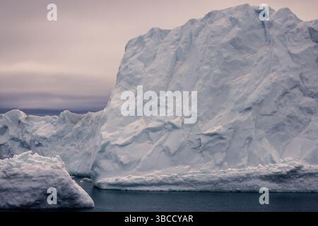 L'imposant iceberg flotte au large de la côte ouest du Groenland sous un ciel crépusculaire polaire doux dans la baie de Baffin. Banque D'Images