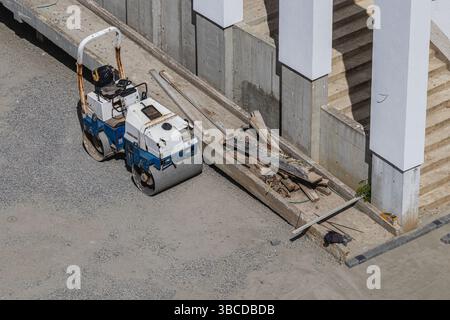 Lviv Ukraine 04.30.25 Un petit rouleau et des matériaux de construction sont sur un site avec du gravier. Le réglage montre les étapes de construction et les travaux inachevés, indic Banque D'Images