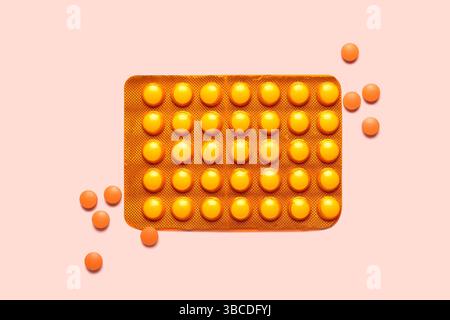 Pilules orange dans le blister sur fond rose Banque D'Images