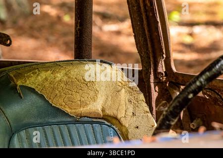 Intérieur d'une voiture abandonnée avec un siège fissuré et endommagé par le soleil et un cadre rouillé, capturant la pourriture, la texture et l'histoire automobile vintage. Banque D'Images