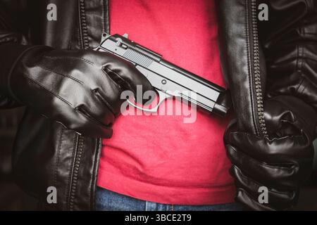 Un homme, policier ou voleur, gangster dissimulant son arme. Le tireur sort une arme à feu sous une veste en cuir noir. Banque D'Images