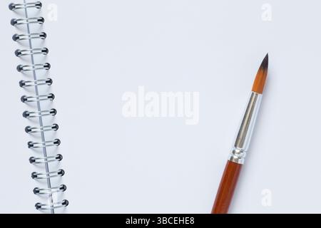 gros plan du pinceau posé sur la page blanche du carnet de croquis aquarelle ouvert Banque D'Images