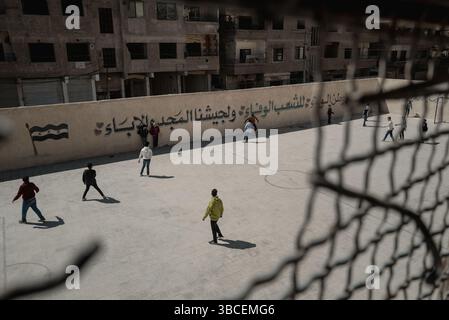 20 mai 2025, Damas, Syrie : DAMAS, SYRIE - 15 AVRIL : des étudiants jouent au football sur le terrain rénové de l'école mixte de Zamalka le 15 avril 2025 à Jobar, Damas, Syrie. Le drapeau à trois bandes fait référence au nouveau régime. Tous les murs de l'école ont été récemment peints pour supprimer les références visuelles à l'ancien président syrien Bachar al-Assad. Jobar, une banlieue de la capitale syrienne Damas, a été pendant des années un front stratégique dans la guerre civile et un emplacement pour les anciennes milices Hay'at Tahrir al-Sham. Avec l’aide de la Russie, la banlieue a été détruite par l’ancien président syrien Bachar All-Assad. (CR Banque D'Images