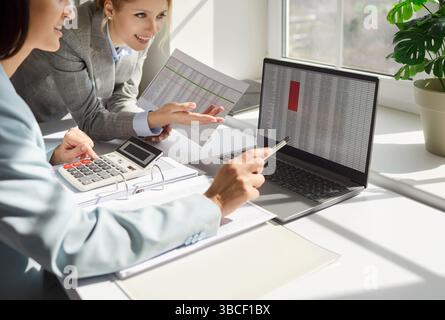 Deux comptables financiers analysant des feuilles de calcul commerciales sur ordinateur portable, assis au bureau Banque D'Images