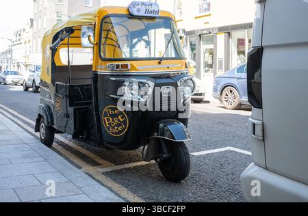 Portrush, Irlande du Nord - 19 mai 2025 : 3 roues Bajaj RE auto rickshaw tuk-tuk en noir et jaune, Port Hotel logo, garé, nouveau transport Banque D'Images