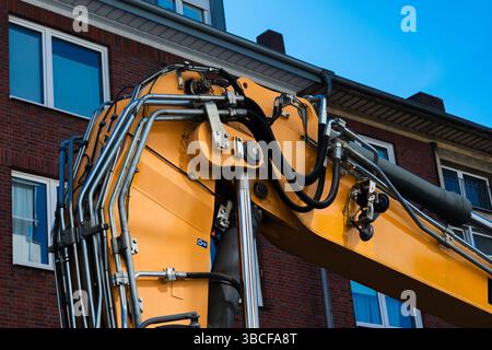 Une pelle jaune vif est positionnée à proximité d'un bâtiment en briques dans un cadre urbain. Les systèmes et mécanismes hydrauliques de la machine sont proéminents Banque D'Images