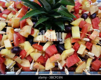 Brochettes de fruits colorées avec pomme, ananas, melon et raisins sur une assiette, parfaites pour des collations saines, des moments rafraîchissants et un plaisir riche en vitamines Banque D'Images