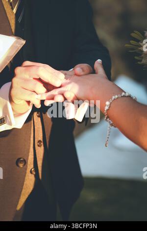 Marié glissant la bande de mariage sur sa main de mariée Banque D'Images
