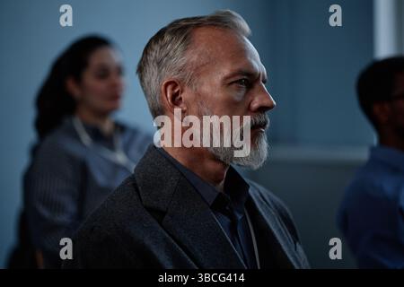Vue latérale d'un homme aîné réfléchi concentré sur la présentation des orateurs tout en assistant à une conférence d'affaires dans la salle de conférence avec éclairage tamisé Banque D'Images