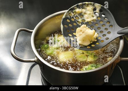 Chou-fleur et brocoli frits enveloppés avec de la pâte à bière dans une casserole avec de l'huile bouillante chaude sur une plaque de cuisson noire, cuisson de fast-food végétalien avec du végétab Banque D'Images