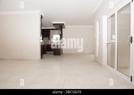 Salon d'une maison neuve qui vient d'être construite comme il est vu du salon vers la cuisine ouverte à côté des portes vitrées qui Banque D'Images