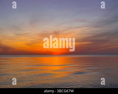Coucher de soleil vibrant sur la mer calme avec des reflets dorés sur l'eau et des formations nuageuses colorées dans le ciel. Banque D'Images
