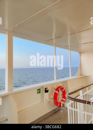 Vue sur l'horizon calme de l'océan au coucher du soleil depuis le pont d'un navire, avec des balustrades blanches et une bouée de sauvetage orange dans le cadre. Banque D'Images