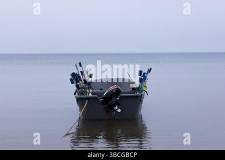 Un petit bateau de pêche gris équipé de drapeaux de signalisation colorés, ancré dans les eaux calmes d'une mer tranquille. Banque D'Images