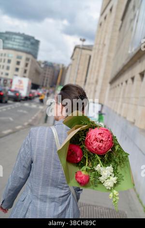 Femme marchant dans la rue de la ville avec un bouquet de fleurs roses dans un emballage vert. Banque D'Images