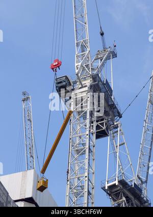 Un groupe de grues de construction hautes travaillant sur un grand site de développement avec une grande structure en béton contre un ciel bleu vif Banque D'Images
