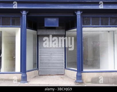 La façade d'une ancienne boutique abandonnée peinte en bleu et blanc avec des fenêtres sales vides devant le magasin et des volets fermés sur la porte Banque D'Images