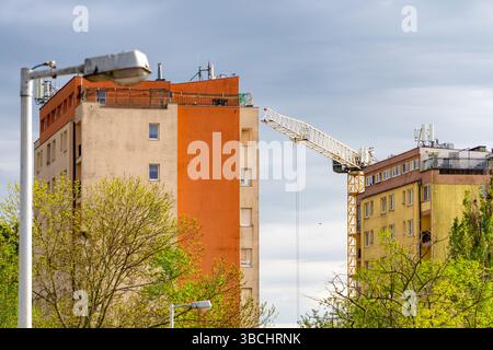 Immeubles d'appartements préfabriqués avec une grue de construction en arrière-plan, entourés d'arbres verts et de lampadaires sous un ciel nuageux. Banque D'Images
