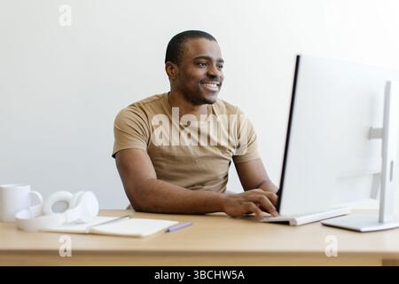 Homme afro-américain souriant travaillant sur un ordinateur de bureau Banque D'Images