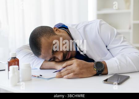 Jeune médecin afro-américain fatigué surmené allongé sur table en clinique Banque D'Images