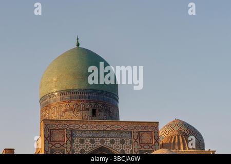 Le dôme turquoise massif et la maçonnerie en mosaïque de la mosquée Bibi-Khanym à Samarcande, en Ouzbékistan, brillent chaleureusement au coucher du soleil sur un ciel dégagé. Banque D'Images