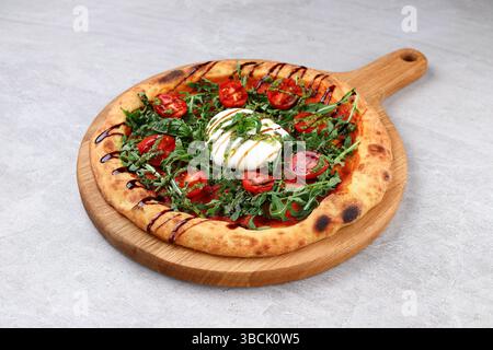 Pizza artisanale garnie de burrata crémeuse, roquette fraîche, tomates cerises, pesto et filet balsamique. Banque D'Images