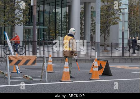 Les ouvriers de la construction restent vigilants au milieu des cônes de circulation tout en guidant le flux matinal avec une matraque rouge Banque D'Images