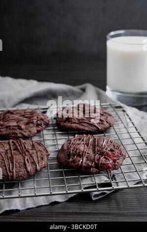 Biscuits aux cerises au chocolat triple avec chips de chocolat et cerises confites : les biscuits aux pépites de chocolat noir arrosent le filet de chocolat noir sur la grille de refroidissement métallique Banque D'Images