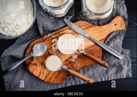 Deux tasses à mesurer nivelées de sucre granulé biologique : directement au-dessus des trois quarts d'une tasse de sucre avec une cuillère, un couteau et d'autres ingrédients de cuisson Banque D'Images