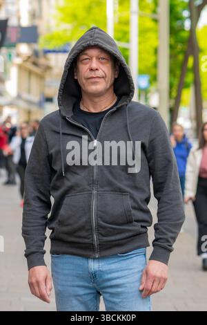 Un homme dans un sweat à capuche gris foncé se tient sur une rue animée de la ville - style de rue et mode décontracté Banque D'Images