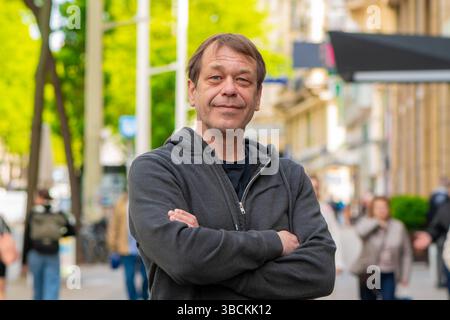 Un homme souriant dans la rue, parmi les piétons et l'architecture urbaine est l'image d'un passant ou d'un citadin Banque D'Images