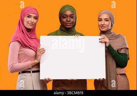 Trois musulmanes tiennent un tableau vierge pour le texte, fond jaune Banque D'Images