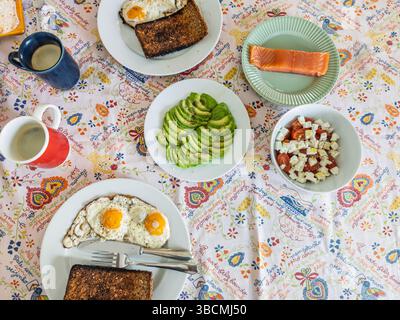 Savourez un brunch maison avec œufs frits, pain grillé, avocat frais, salade de fromage et saumon fumé, idéal pour une matinée paresseuse. Banque D'Images