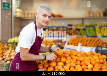 Travailler dans un supermarché - vendeur masculin trie des mandarines mûres sur la vitrine Banque D'Images
