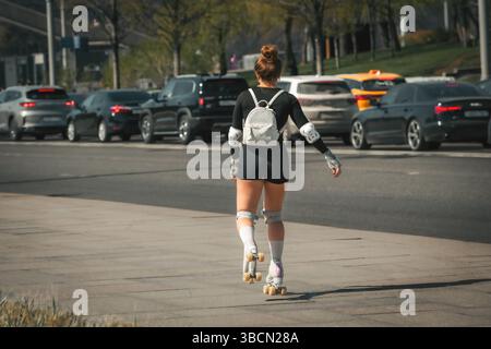 femme avec sac à dos sur patins à roulettes chevauchant sur le trottoir Banque D'Images