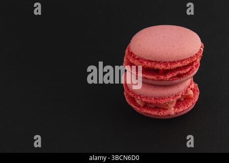 Les macarons roses sont empilés de manière attrayante sur un fond sombre, mettant en valeur leur texture lisse et leur couleur vibrante, parfaits pour les amateurs de desserts et spéciaux Banque D'Images