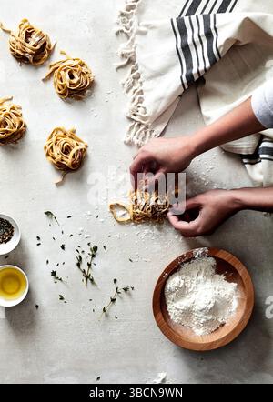 Mains façonnant des nids de pâtes fraîches sur une surface farinée avec des herbes Banque D'Images