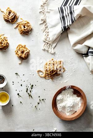 Mains façonnant des nids de pâtes fraîches sur une surface farinée avec des herbes Banque D'Images