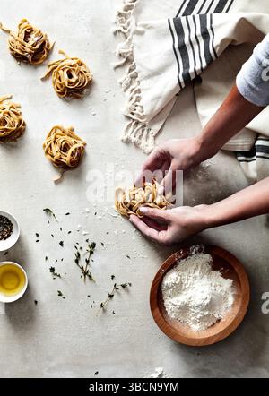 Mains façonnant des nids de pâtes fraîches sur une surface farinée avec des herbes Banque D'Images