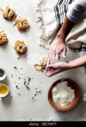 Mains façonnant des nids de pâtes fraîches sur une surface farinée avec des herbes Banque D'Images
