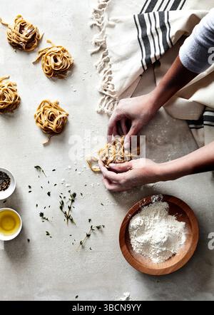 Mains façonnant des nids de pâtes fraîches sur une surface farinée avec des herbes Banque D'Images