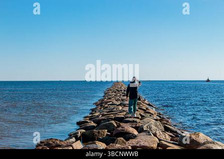 La femme marche sur la taupe de la rivière Pärnu en été. Jetée en pierre populaire dans la ville de Pärnu en Estonie. Banque D'Images
