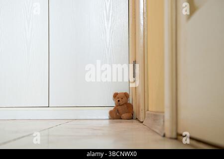 Abandonné bébé ours en peluche brun se trouve dans le coin par la porte de l'appartement sur le sol, jouet pour bébé Banque D'Images