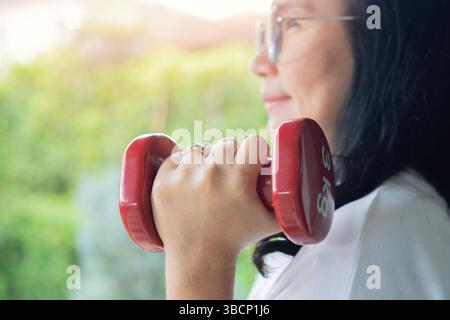 Vue latérale rapprochée d'une dame mature soulève des haltères bleus maintenant la forme physique à l'extérieur le matin. Banque D'Images